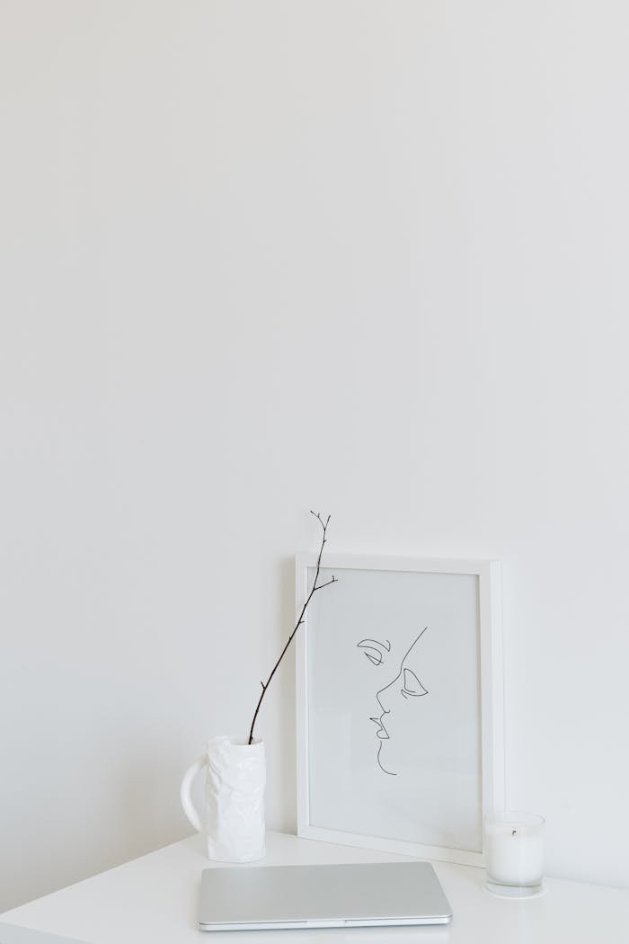 Sleek minimalist decor featuring a laptop, framed art, and ceramic vase on a white table.